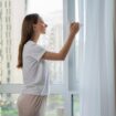 Pretty young woman opens a window at home, ventilating the room.